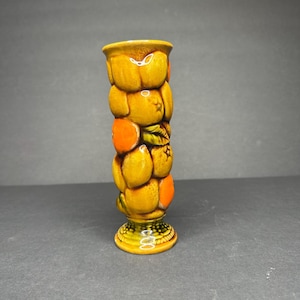 May include: A ceramic vase with a textured design of oranges and leaves. The vase is primarily yellow and orange, with green accents on the base and leaves. The vase has a pedestal base and a flared top.
