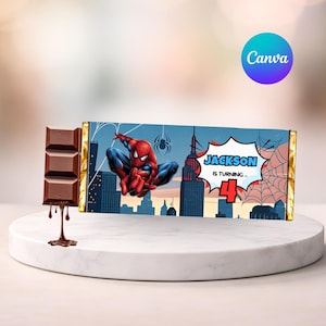 Peut inclure: Une barre de chocolat sur le thème de Spiderman. L'emballage présente Spiderman dans une pose dynamique sur fond de paysage urbain. Le texte sur l'emballage indique "Jackson a 4 ans". La barre de chocolat est partiellement déballée, avec du chocolat fondu qui coule.