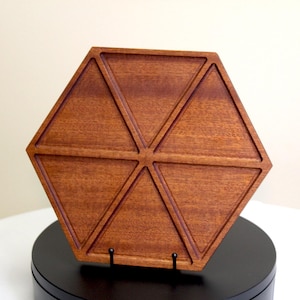 May include: A hexagonal wooden tray with a rich brown finish. The tray is divided into six triangular sections by carved lines. The tray is displayed on a black stand against a neutral background. The wood grain is visible.