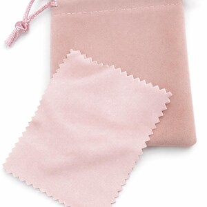 May include: A light pink velvet drawstring pouch with a matching pink satin cleaning cloth. The pouch has a knotted drawstring closure. The cleaning cloth has a zig-zag edge.