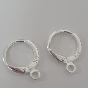 May include: Two silver-colored leverback earring findings. Each finding has a rounded hoop with a hinged lever and a small loop at the bottom for attaching a charm or earring component. The findings are set against a light gray background.