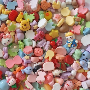 Könnte beinhalten: Eine bunte Auswahl an kleinen, dekorativen Harz-Anhängern in verschiedenen Formen, darunter Blumen, Sterne, Tiere und Lebensmittel. Die Anhänger sind in den Farbtönen Rosa, Gelb, Blau, Grün und Orange gehalten und erzeugen eine verspielte und skurrile Ästhetik.