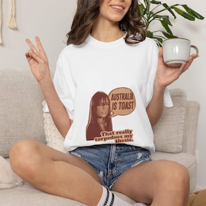 Peut inclure: T-shirt blanc avec un graphisme d'une femme et le texte "AUSTRALIA IS TOAST" dans une bulle de dialogue. Le texte "That really torpedoes my thesis" est en dessous.