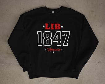 Op de afbeelding: Zwart sweatshirt met de rode tekst "LIB", het witte nummer "1847" en "= Monrovia =" eronder. De tekst heeft een collegiale stijl. Het sweatshirt wordt gepresenteerd tegen een neutrale achtergrond.