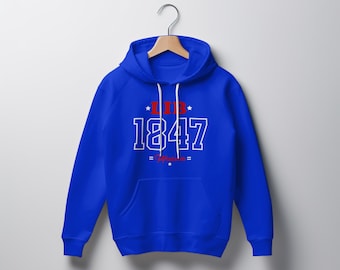 Op de afbeelding: Een koningsblauwe hoodie met een wit trekkoord en een voorzak. De hoodie heeft de tekst "LIB 1847" in het wit, met rode accenten en sterdetails. De hoodie hangt aan een houten hanger.