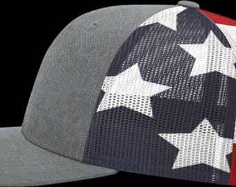 Op de afbeelding: Een baseballpet met een effen grijs voorpaneel en een grijze klep. De zij- en achterpanelen zijn gemaakt van mesh-materiaal met een patriottisch patroon van witte sterren op een marineblauwe achtergrond en horizontale rode en witte strepen.