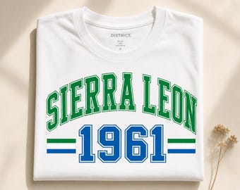 Op de afbeelding: Een wit T-shirt met korte mouwen met de tekst SIERRA LEONE in een groen gebogen collegiaal lettertype boven de blauwe tekst 1961. Het ontwerp bevat twee horizontale strepen in groen, wit en blauw aan weerszijden van het jaartal 1961.