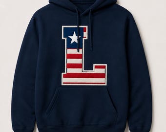 Op de afbeelding: Een marineblauwe hoodie met lange mouwen en een grote, centraal geplaatste letter L als applicatie. De letter is ontworpen met een rood, wit en blauw vlagpatroon, inclusief een blauw vierkant met een witte ster en horizontale rode en witte strepen.