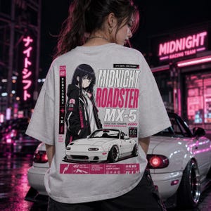 Puede incluir: Una camiseta gris claro con un gráfico de un personaje de estilo anime y un coche deportivo blanco. El texto "MIDNIGHT ROADSTER MX-5" está en rosa y blanco. La camiseta también incluye texto japonés y las palabras "OWN THE STREETS."