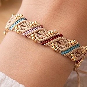 May include: A macrame bracelet with a beige base, accented with gold beads and sections of red, blue, and pink thread. The bracelet is on a wrist, showing the intricate woven design and adjustable tie closure.