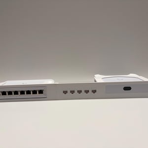 Puede incluir: Un dispositivo blanco de montaje en rack de red con múltiples puertos y conectores. El dispositivo tiene una serie de puertos rectangulares a la izquierda y una serie de puertos redondos a la derecha. Diseñado para infraestructura de red.