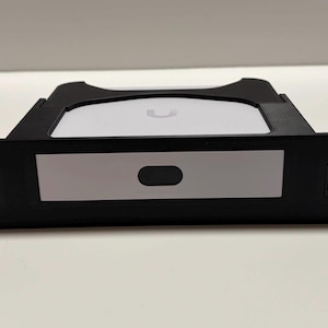 Op de afbeelding: Zwart netwerk rack mount met twee RJ45-poorten aan elke kant. Het midden heeft een wit paneel met een zwarte ovale knop en een wit apparaat met een logo. De rack mount is ontworpen om netwerkapparatuur te bevatten.