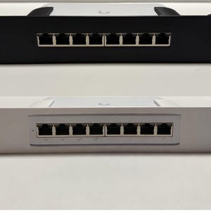 May include: Two network switches, one black and one white, are displayed. Each switch has eight Ethernet ports and is designed for rack mounting. The switches are shown against a white background.