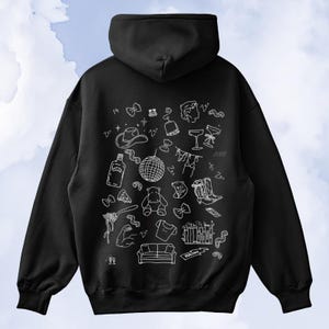 May include: Black hoodie with a white doodle design. The design includes a cowboy hat, disco ball, cocktail glasses, and other illustrations. The hoodie has a hood and long sleeves.