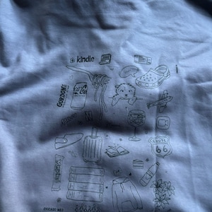 May include: Gray sweatshirt with a collection of illustrated icons including a Kindle, Coca-Cola can, pasta, a dog, a shoe, an airplane, a Route 66 sign, and more. The text "CHICAGO MED" is at the bottom.