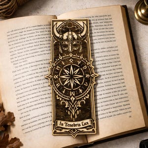 May include: Wooden bookmark with a Viking helmet design, a compass rose, and the Latin phrase "In Tenebris Lux." The bookmark is rectangular with intricate laser-cut details and is resting on an open book.