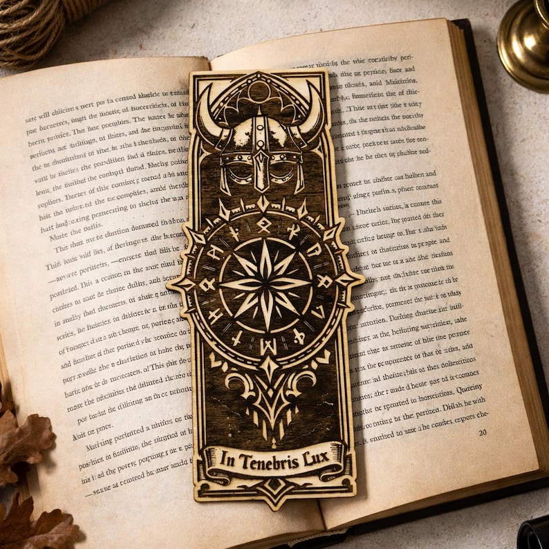 May include: Wooden bookmark with a Viking helmet design, a compass rose, and the Latin phrase "In Tenebris Lux." The bookmark is rectangular with intricate laser-cut details and is resting on an open book.