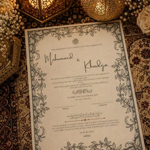 May include: A formal wedding certificate with the names "Muhammed & Khadija" in elegant script. The document is bordered with floral designs and includes text in English and Arabic. The certificate is on a patterned surface, with decorative lanterns in the background.