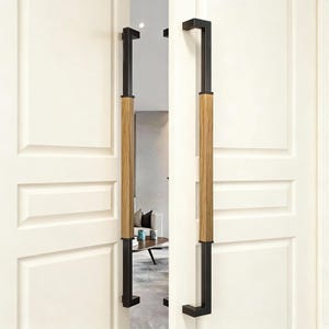 Peut inclure: Portes doubles blanches avec des poignées de porte en métal noir et bois. Les poignées ont une forme rectangulaire avec une section centrale en bois et des extrémités en métal noir. Les portes ont un design à panneaux.