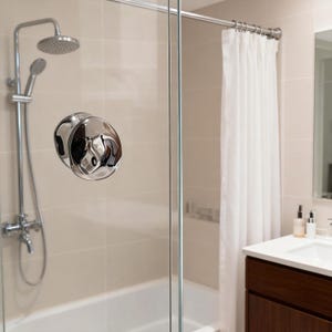 May include: A modern bathroom shower setup featuring a chrome shower head, handheld shower, and a polished chrome door handle. The shower is enclosed by a glass door, with a white curtain and a vanity in the background.