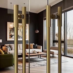 Peut inclure: Gros plan sur des poignées de porte dorées dans un intérieur moderne. Les poignées cylindriques ont une prise texturée et sont montées sur une porte vitrée. L'arrière-plan montre un salon avec un canapé, des œuvres d'art et de la lumière naturelle.