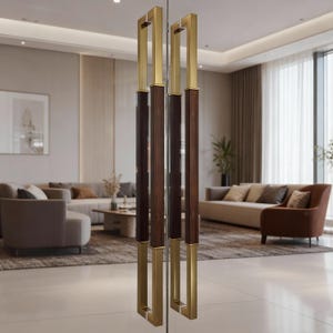 Peut inclure: Une paire de poignées de porte en verre modernes. Les poignées présentent un design rectangulaire avec un cadre en métal doré et un centre en bois brun foncé. Les poignées sont installées sur une porte vitrée, avec un salon visible en arrière-plan.