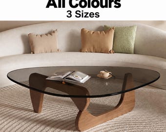 Könnte beinhalten: Ein Couchtisch mit einer dreieckigen, dunkel getönten Glasplatte und einem hellen Holzgestell. Der Text "All Colours 3 Sizes" ist oben sichtbar. Ein aufgeschlagenes Buch und eine kleine Tasse auf einer Untertasse stehen auf der Glasfläche.