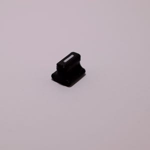 Peut inclure: Un petit composant en plastique noir avec une base rectangulaire et un dessus arrondi surélevé. Un détail rectangulaire blanc est visible sur le dessus. L'objet est posé sur un fond clair et uni.