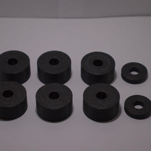 Pode incluir: Um conjunto de oito pés de borracha pretos com uma superfície texturizada. Os pés são cilíndricos com um furo central, projetados para serem usados como almofadas para móveis ou outras aplicações.