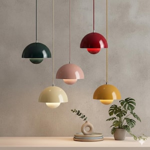 May include: Five pendant lights in various colors: dark green, pink, cream, red, and yellow. Each light has a rounded, dome-shaped shade and a spherical light source. The lights hang from thin cords, creating a modern and stylish lighting arrangement.