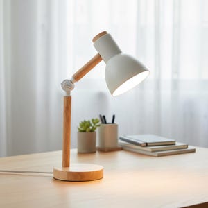 May include: A white desk lamp with a wooden base and arm. The lamp has a conical shade and is positioned on a light-colored wooden desk. A small succulent plant and a pen holder are visible in the background.