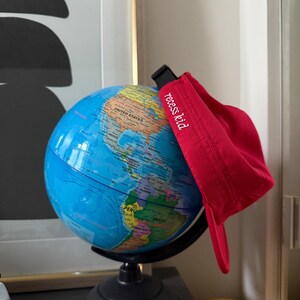 May include: A blue and black globe with a red visor hat that says "recess kid" in white text. The globe is on a black stand. The hat is made of a corduroy material.