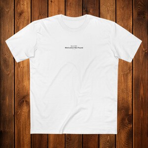 May include: Two white t-shirts are folded and stacked. The top shirt has the text "Error 404: Motivation Not Found" printed in black. The shirts are made of a soft material, likely cotton, and are neatly presented.