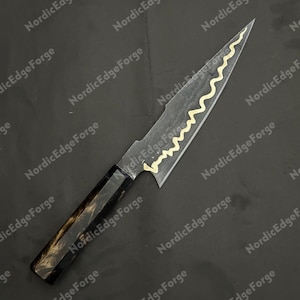 K&ouml;nnte beinhalten: Ein handgefertigtes Messer mit dunkler Klinge und einem dekorativen goldenen Wellenmuster. Der Griff ist schwarz und braun. Der Text "NordicEdgeForge" ist im Hintergrund sichtbar.