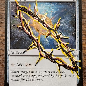 May include: A Sol Ring card featuring a detailed illustration of a spiky, golden ring-like structure. The card has the text "Artifact" and flavour text about a mysterious crater. The background of the card is a cosmic scene.
