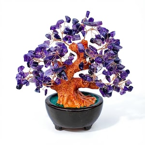 Puede incluir: Un árbol decorativo de piedras preciosas de amatista en una maceta de cerámica negra. El árbol presenta un tronco y ramas marrones con virutas de amatista moradas cableadas a las ramas. La maceta tiene un interior verde y está sobre un fondo blanco.