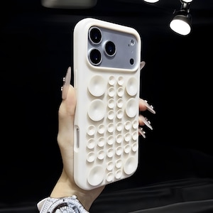May include: A white phone case with a textured design of raised circles. The case has a camera cutout and a smooth, matte finish. The phone case is held in a hand.