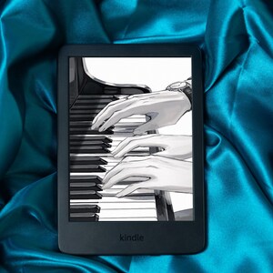 Puede incluir: Un lector de libros electrónicos Kindle negro que muestra una ilustración en blanco y negro de manos tocando el piano. El lector de libros electrónicos está sobre un fondo de tela de satén turquesa. La palabra "kindle" está impresa en la parte inferior del lector.