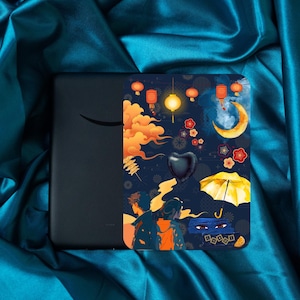 May include: A black e-reader with a decorative cover featuring a dark blue background with orange clouds, red lanterns, and a yellow crescent moon. The cover also has a black heart-shaped balloon and a yellow umbrella.
