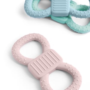 May include: Two baby teethers in the image. One is light pink, the other is light blue and teal. Each teether has a figure-eight shape with a textured surface and a rectangular center section.