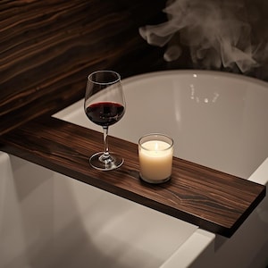 May include: A dark wood bath tray holds a wine glass filled with red wine and a lit candle in a glass. The tray sits across a white bathtub, with steam rising in the background.