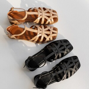 May include: Two pairs of sandals. The top pair is tan with a woven design and brown soles. The second pair is also tan with a woven design and brown soles. The bottom pair is black with a woven design and black soles. The fourth pair is black with a woven design and black soles.