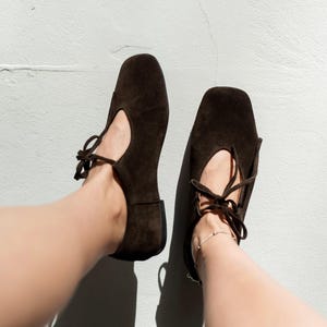 Side view of white minimalist leather sneakers with a flexible ivory sole, styled with dark denim jeans