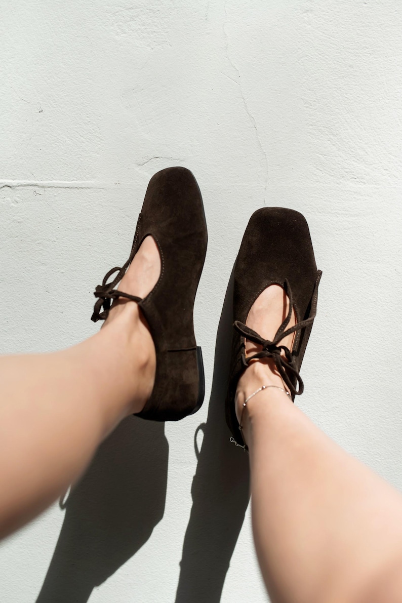 Side view of white minimalist leather sneakers with a flexible ivory sole, styled with dark denim jeans