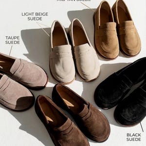 May include: A collection of suede loafers in various colors, labeled as Taupe Suede, Light Beige Suede, Mid-Tan Suede, Dark Brown Suede, and Black Suede. Each pair features a classic penny loafer strap across the vamp and a rounded toe design.