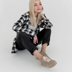 Pu&ograve; includere: Una persona indossa una maglietta bianca, jeans neri e una camicia a quadri bianchi e neri. La persona indossa anche scarpe da ginnastica beige con lacci bianchi. L'outfit &egrave; casual e comodo.