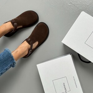 May include: A pair of brown suede shoes with a T-strap design. The shoes are dark brown and have a buckle closure. Two white boxes with the brand name "Maletskiy" are also in the image.