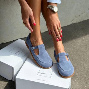 May include: Light blue suede Mary Jane style shoes with a buckle closure and a brown sole. The shoes are displayed on top of white boxes. The brand name "Maletskiy" is printed on the boxes.