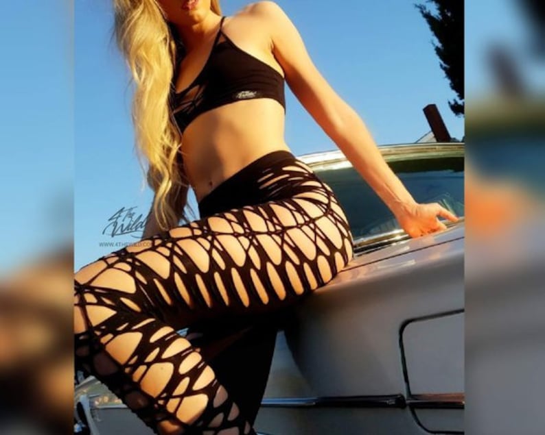 Pode incluir: Uma mulher vestindo um top curto preto e leggings de rede preta posa em um carro vintage. As leggings t&ecirc;m um design recortado.