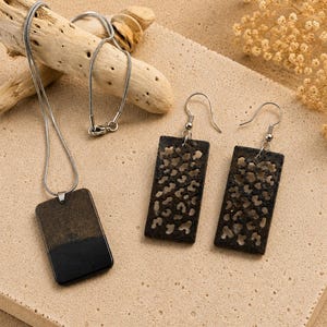 May include: A jewelry set consisting of a necklace and a pair of earrings. The necklace features a rectangular pendant with a black and metallic bronze finish on a silver-toned chain. The matching earrings are rectangular with a cutout leopard print.